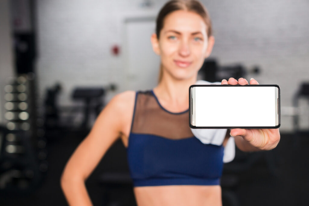 Fit woman in sportswear holding smartphone with blank screen at the gym