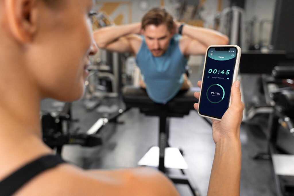 Woman holding smartphone with workout timer app while man performs back