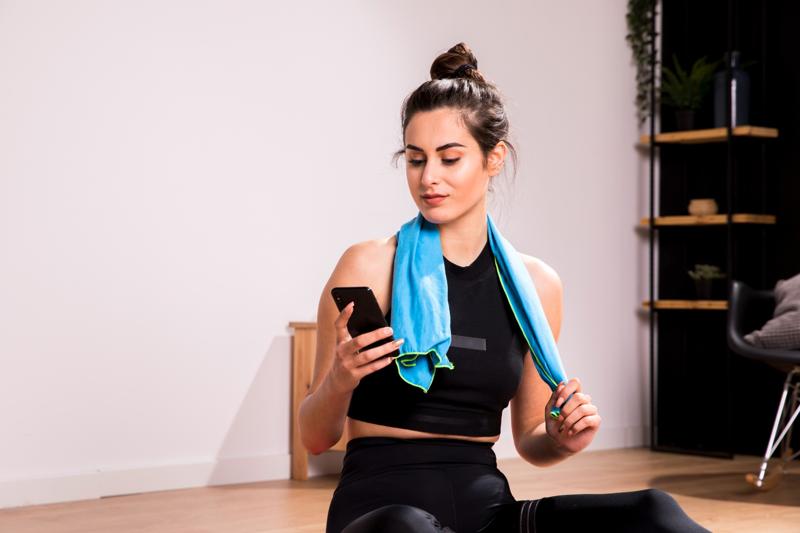 Freeletics App Review: Fitness woman sitting on floor using mobile phone after workout