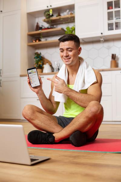 FitBudd Review: Fitness coach sitting on yoga mat, smiling and holding smartphone showing FitBudd app.