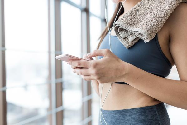 Trainerize Review: Woman in workout clothes using smartphone with towel on shoulder, fitness tracking app concept.