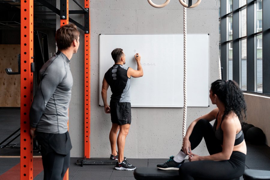 Personal trainer explains workout strategy on whiteboard to clients during a gym session
