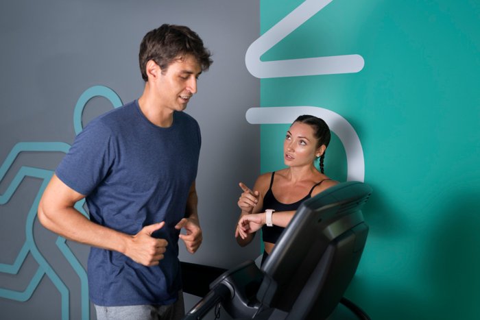 A personal trainer coaching a man while he runs on a treadmill, giving instructions and monitoring his progress during a gym session.