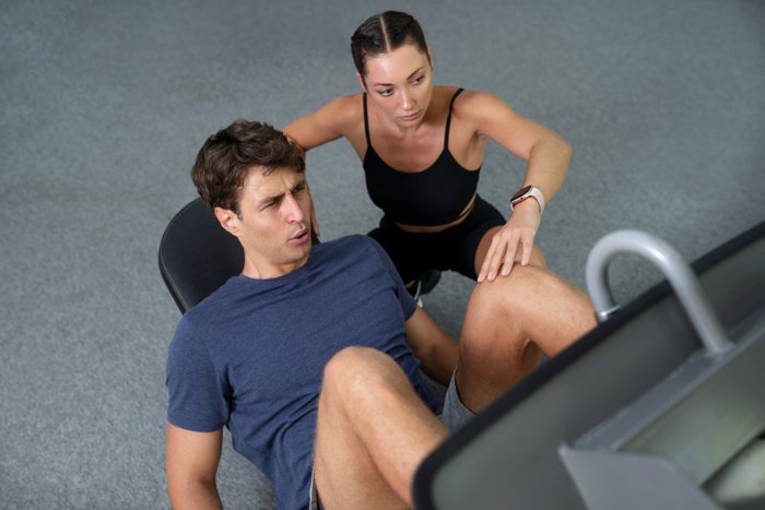 A personal trainer coaching a man on a leg press machine at the gym, offering support and motivation during an intense workout.