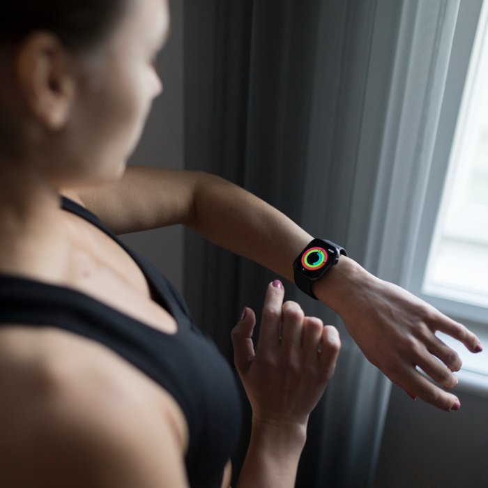 TrueCoach App Review: A woman in sportswear checking her fitness progress on a smartwatch with activity rings, standing near a window post-workout.