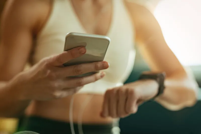 Woman in a sports bra checking her smartphone and fitness watch, likely during a workout.