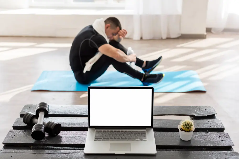 PT Distinction 2025 Review Online fitness coaching setup with laptop, dumbbells, and resting personal trainer in background – representing a digital personal training business environment
