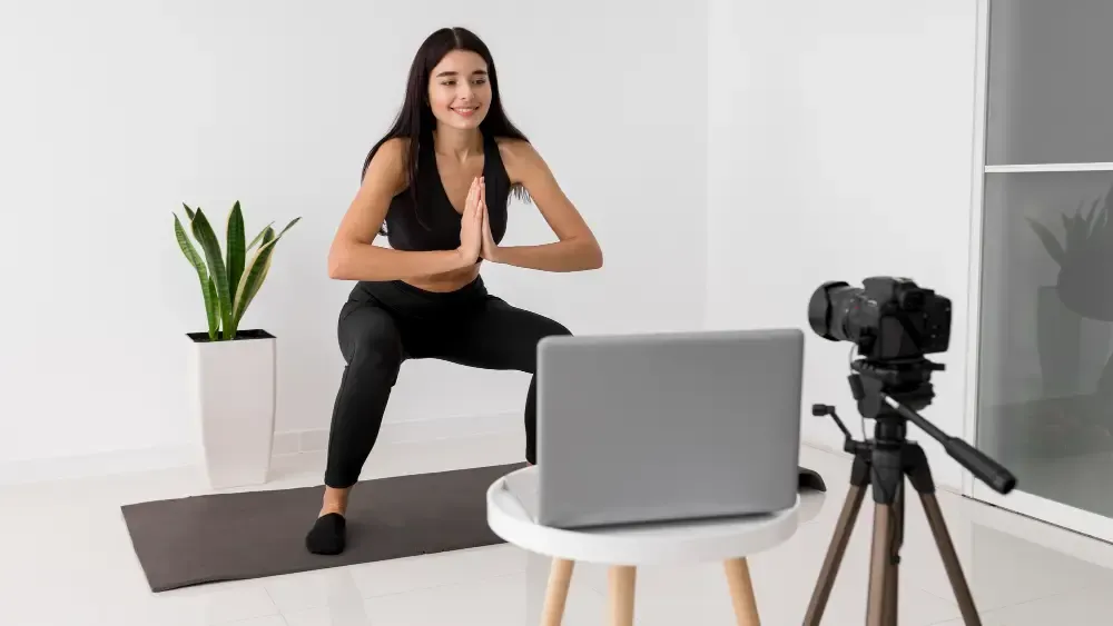 Female personal trainer demonstrating squat exercise during online home workout session
