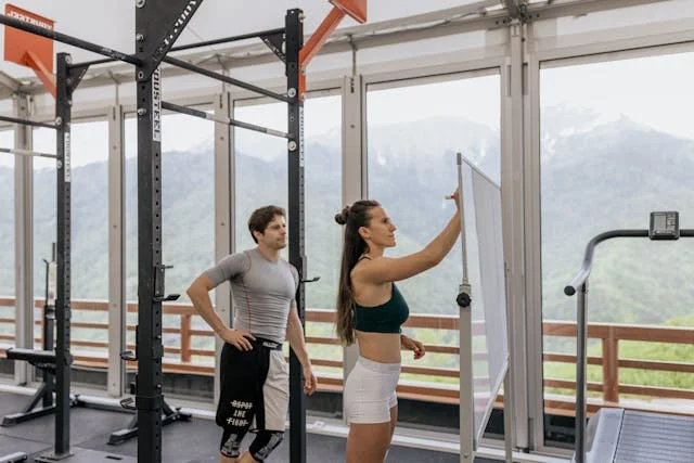 HubFit Review: Two fitness trainers in a gym with scenic mountain view, planning a workout on a whiteboard