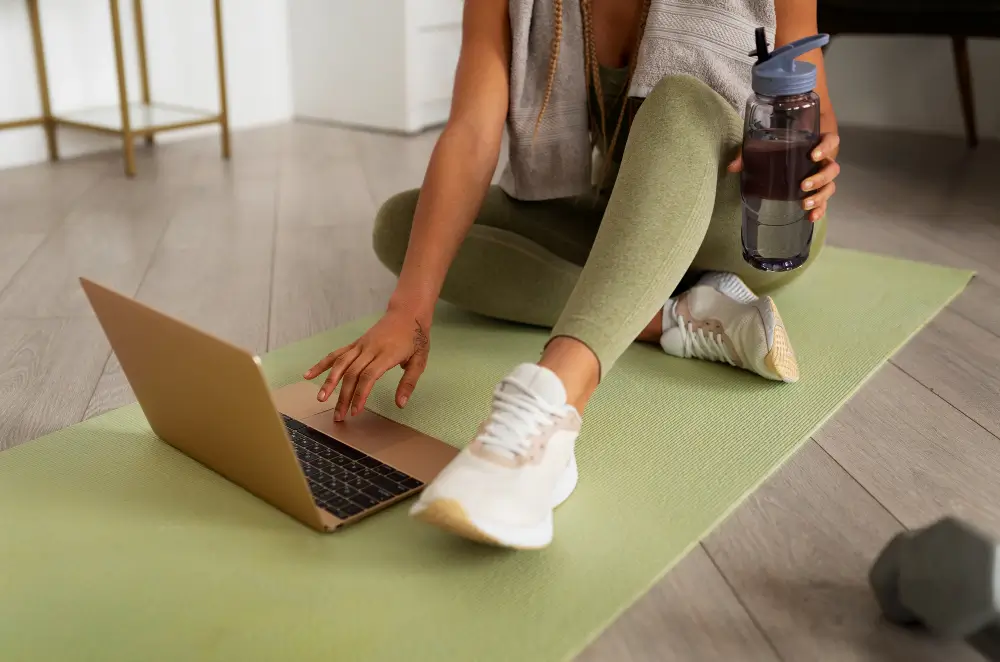 Personal trainer using laptop on yoga mat with PT Distinction coaching software