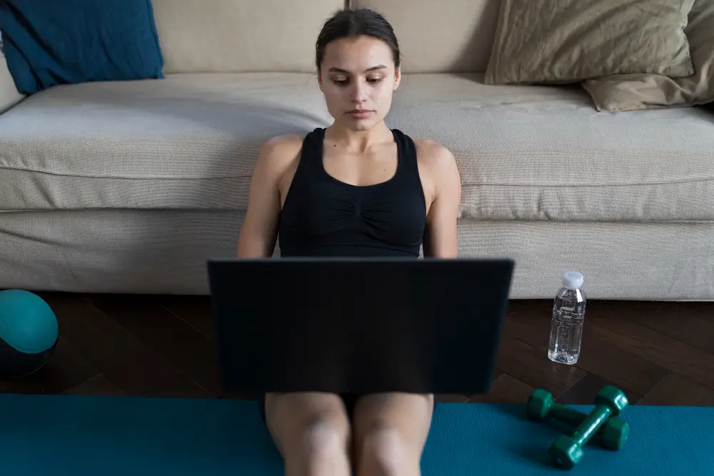 Female athlete exercising at home while following digital fitness program on laptop.