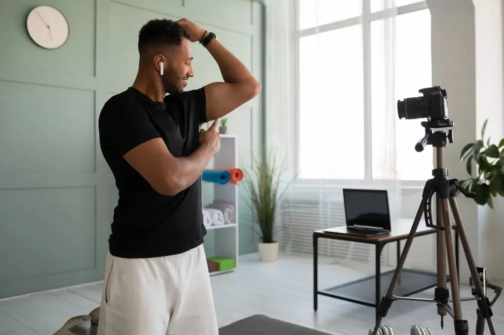 Fitness coach recording a workout video at home while flexing arm muscles in front of camera